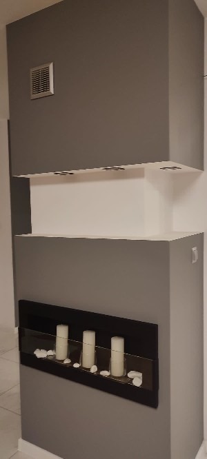 Szara ściana z wnęką na świece i półkami, minimalistyczny design, wykończenie wnętrza.