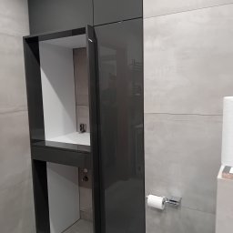 Usługi stolarskie Lazar Piotr - Nowoczesna szafka łazienkowa w odcieniach szarości z otwartą półką i błyszczącymi frontami, dopasowana do płytek na ścianie. Minimalistyczny design.