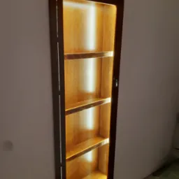 Wnęka ścienna z drewnianą, podświetloną półką, widoczna z boku. Ciemna rama i cztery półki z ciepłym oświetleniem tworzą unikalny element dekoracyjny.