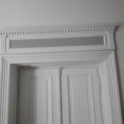 Białe, klasyczne drzwi z dekoracyjną ażurową listwą wentylacyjną nadproża. Dwoje drzwi panelowych z ozdobnymi listwami i pilastrami.