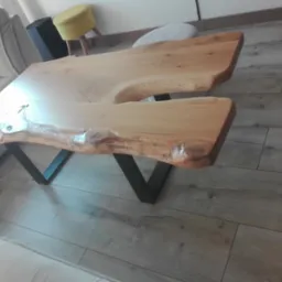 Stolik kawowy z blatem z litego drewna o nieregularnym kształcie, oparty na metalowych nogach w kształcie litery V. Widoczne usłojenie drewna i naturalne krawędzie.