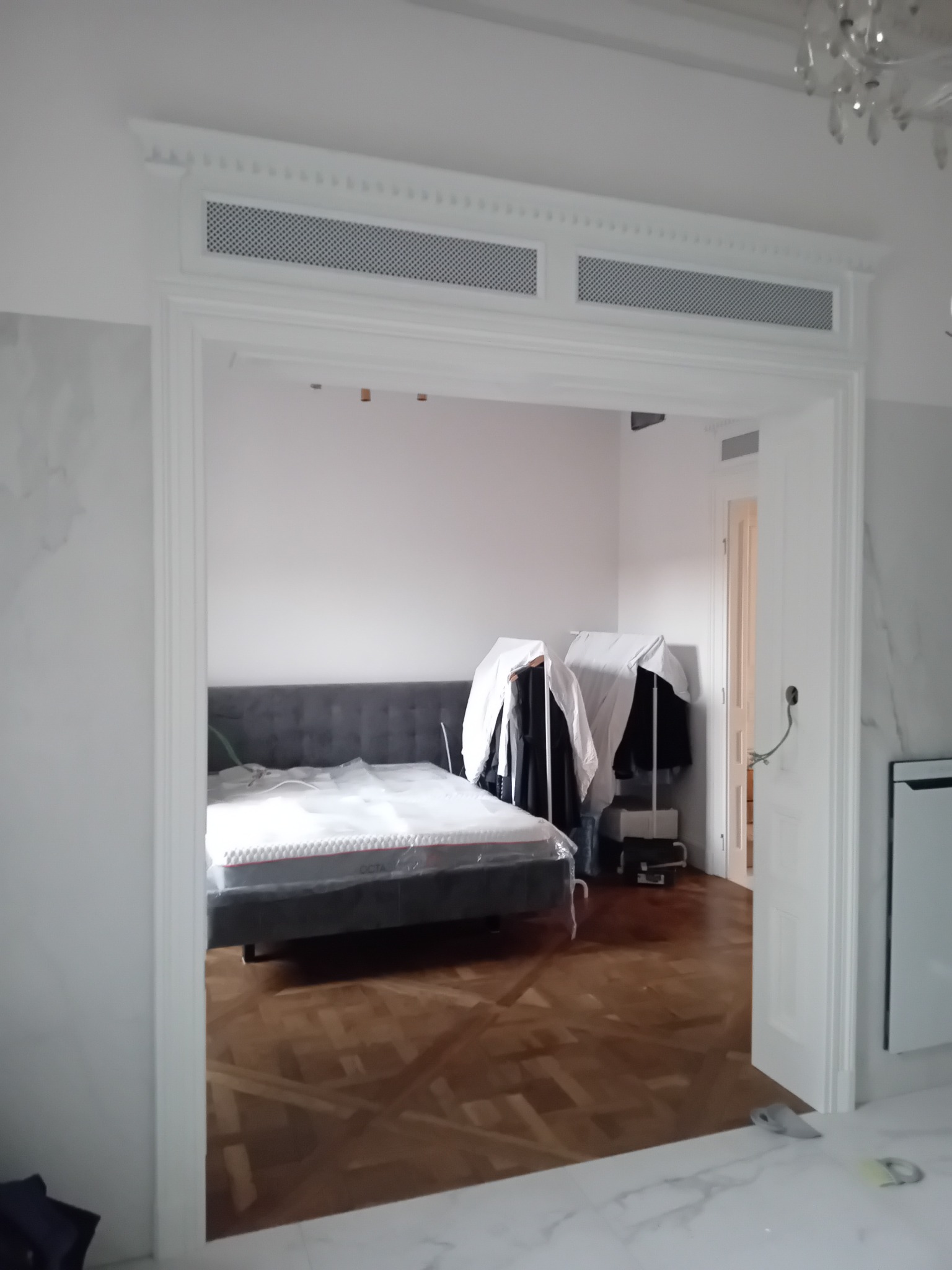 Eleganckie, białe drzwi drewniane z ozdobną kratką wentylacyjną w Czarkowie, prowadzące do sypialni z parkietem i łóżkiem. Widoczne detale wykończenia.