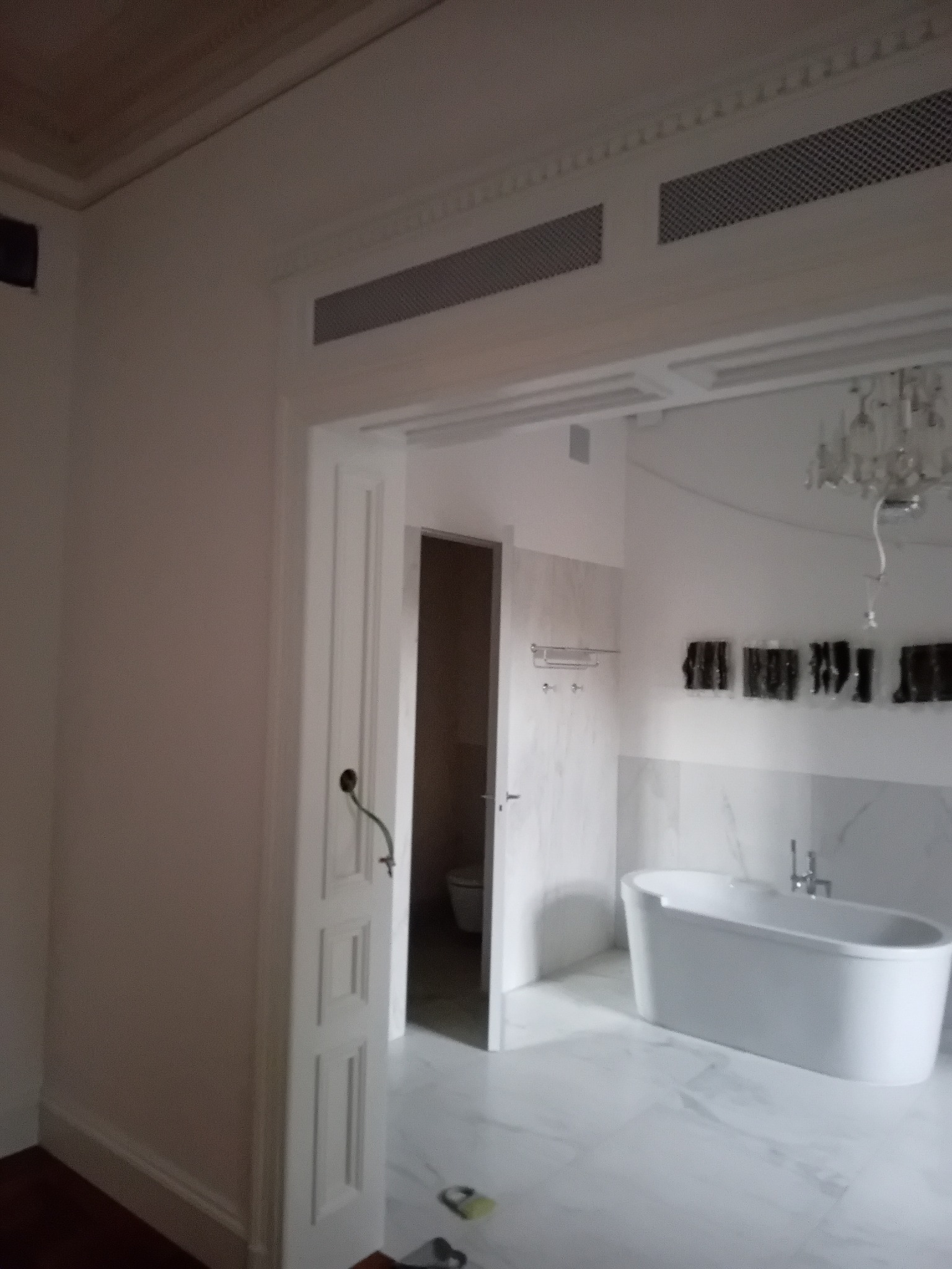 Nowoczesna łazienka z białą wolnostojącą wanną, marmurowymi płytkami i otwartymi drzwiami, ukazująca minimalistyczny design i eleganckie wykończenie.