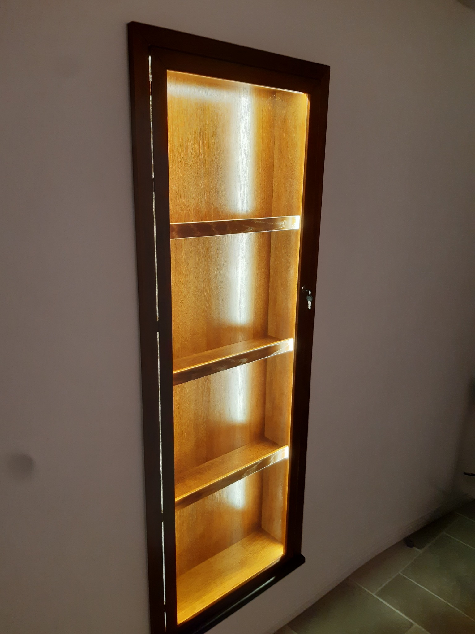 Wnęka ścienna z drewnianą, podświetloną półką, widoczna z boku. Ciemna rama i cztery półki z ciepłym oświetleniem tworzą unikalny element dekoracyjny.