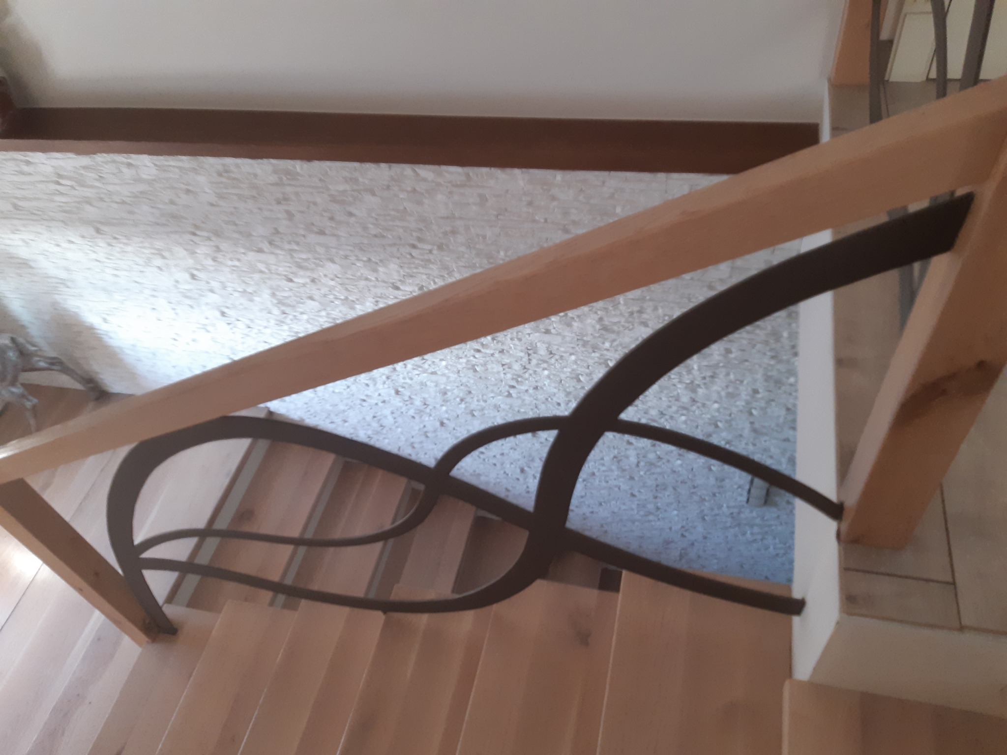 Drewniane schody z ozdobną, metalową balustradą w Czarkowie. Ujęcie z góry, ukazujące detale konstrukcji i wzór balustrady.