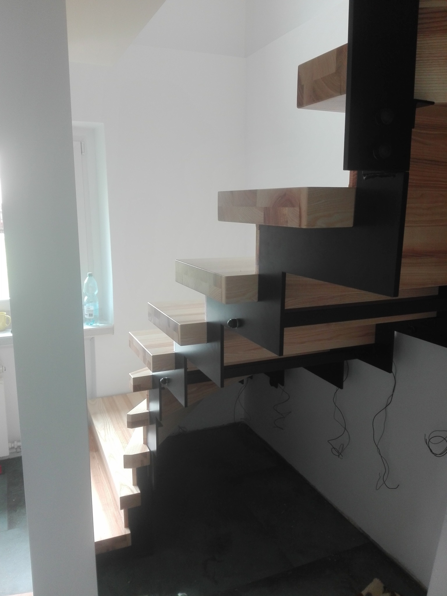 Nowoczesne schody drewniane z czarnymi metalowymi elementami mocującymi, widok z dołu, oświetlenie dzienne, surowy stan wykończenia wnętrza.