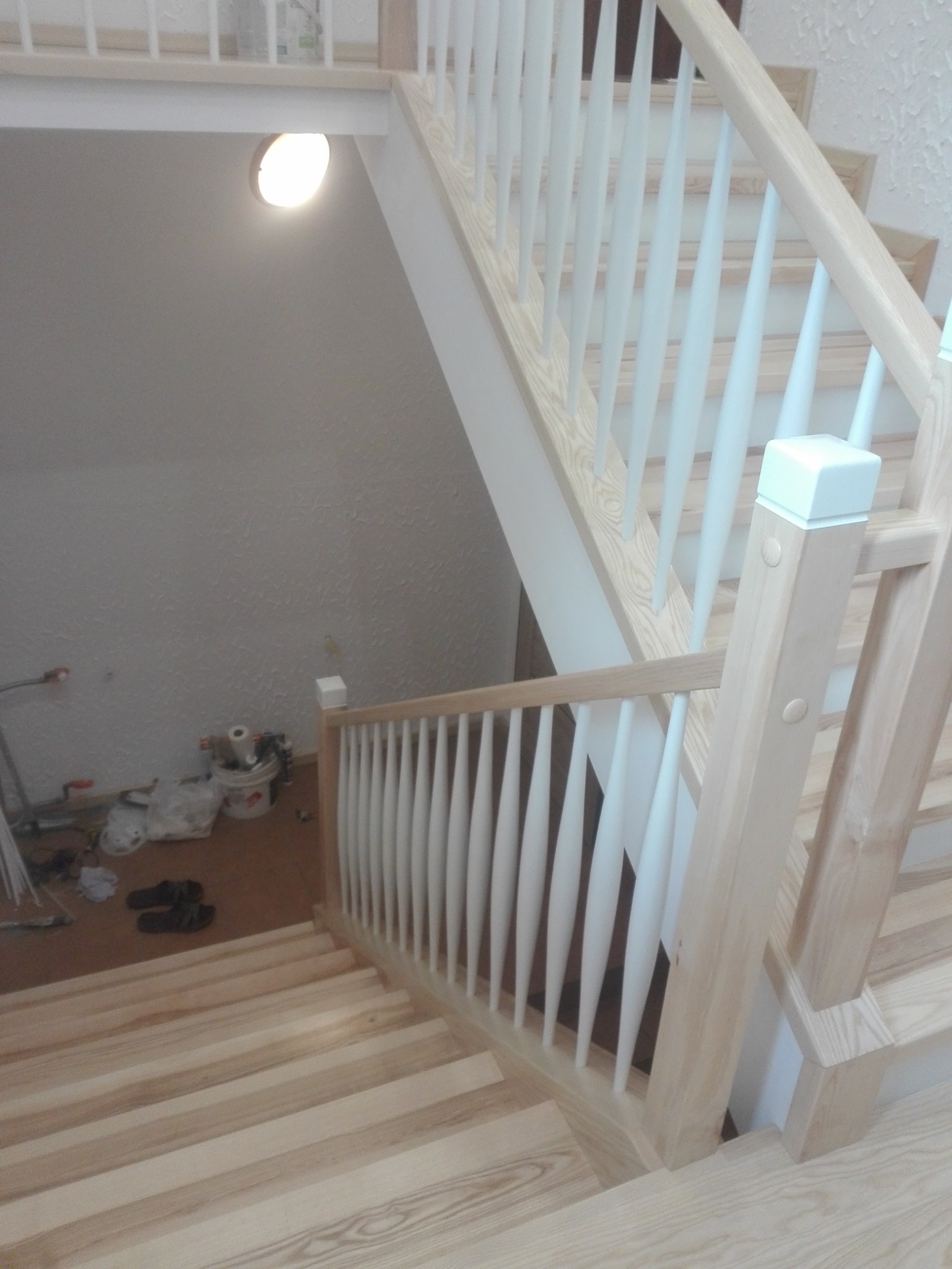 Jasne, drewniane schody z białymi balustradami. Widoczne narzędzia i materiały budowlane w tle, sugerujące trwający montaż. Ujęcie z góry, na pierwszym planie stopnie.