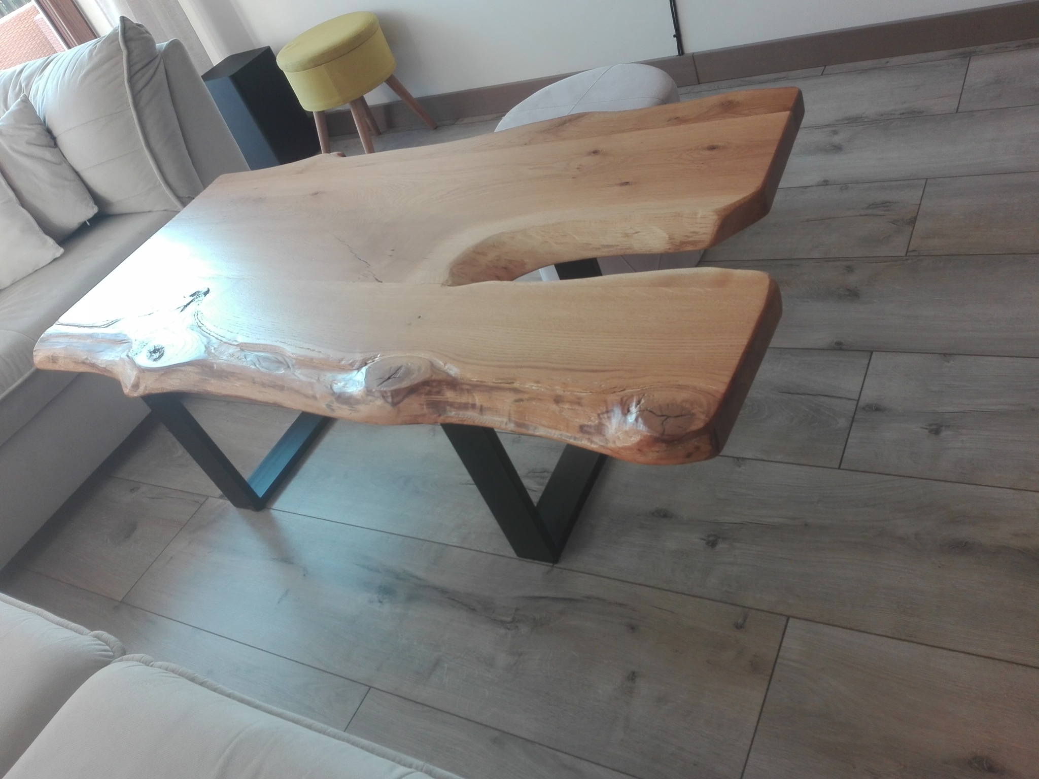 Stolik kawowy z blatem z litego drewna o nieregularnym kształcie, oparty na metalowych nogach w kształcie litery V. Widoczne usłojenie drewna i naturalne krawędzie.