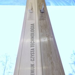 Klein - Okno PCV z widoczną różnicą czystości: prawa strona brudna, lewa świeżo umyta, z logo firmy 'EMLUK - CZYSTA TECHNOLOGIA' na ramie okiennej.