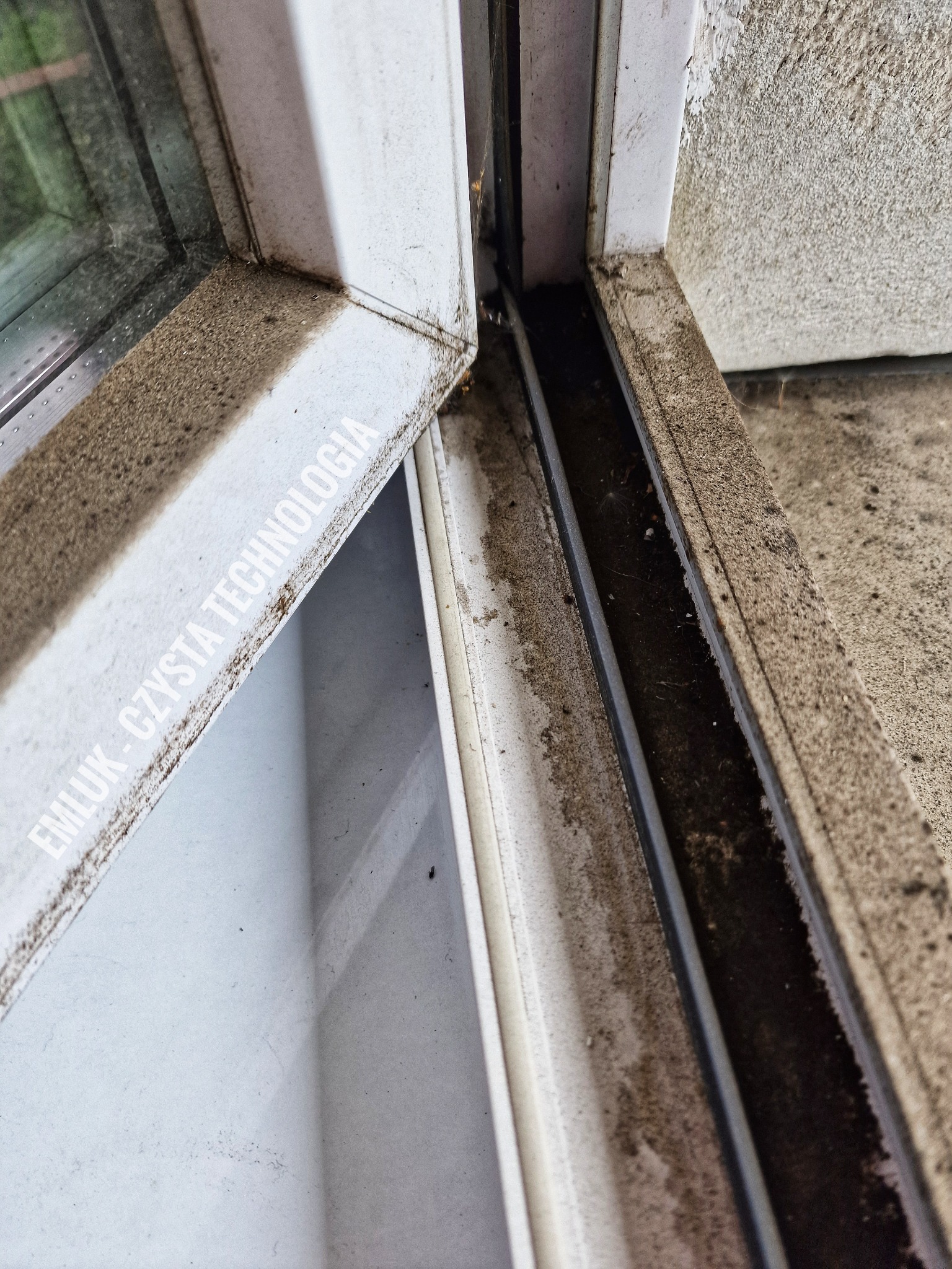 Silnie zabrudzony, otwarty fragment okna PCV z widocznymi resztkami kurzu i brudu w uszczelkach i prowadnicach, z logo firmy sprzątającej. Widoczne zacieki i osad.