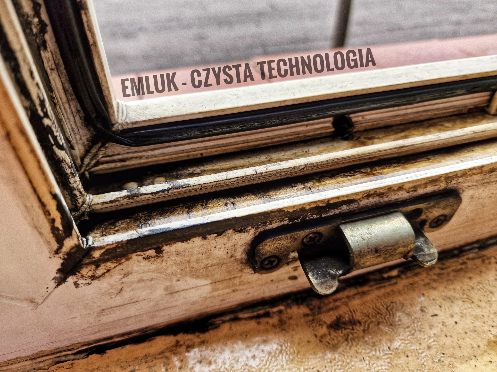 Bardzo brudne, stare okno z widocznym zardzewiałym zamkiem i napisem 'EMLUK - CZYSTA TECHNOLOGIA'.