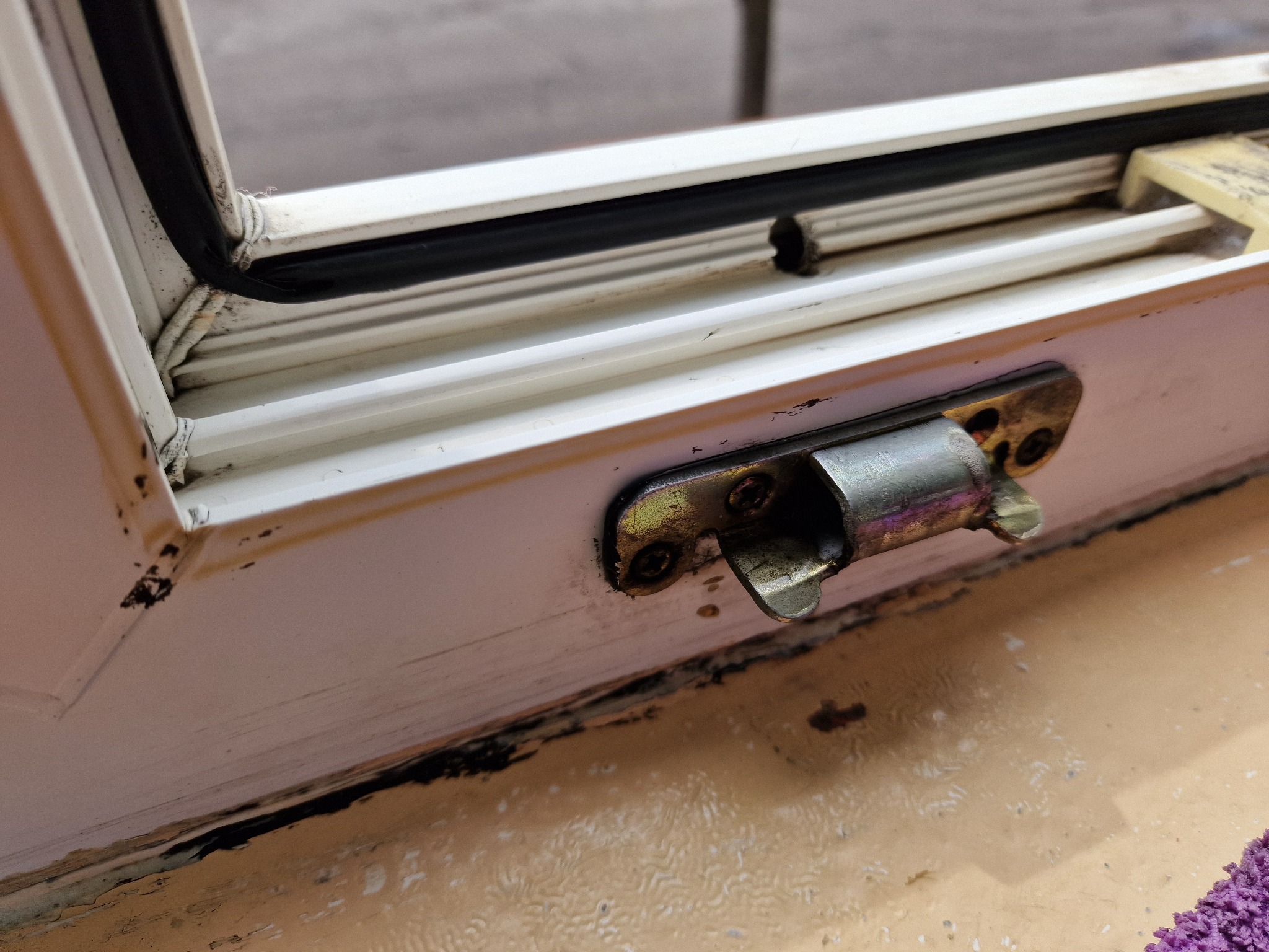 Brudne, białe okno z metalowym zamknięciem, widoczne ślady pleśni i zabrudzeń na framudze.