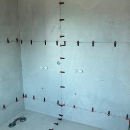 Taurus Bud - Montaż płytek wielkoformatowych w łazience z użyciem systemu poziomowania, widoczne przyssawki do przenoszenia płytek i krzyżyki dystansowe.