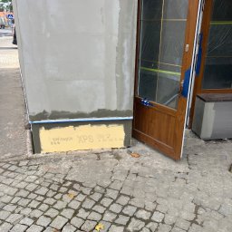 Taurus Bud - Otwarta, drewniana stolarka okienna zabezpieczona folią i taśmą, obok ocieplona i otynkowana ściana zewnętrzna z widocznymi płytami izolacyjnymi Swissport XPS.