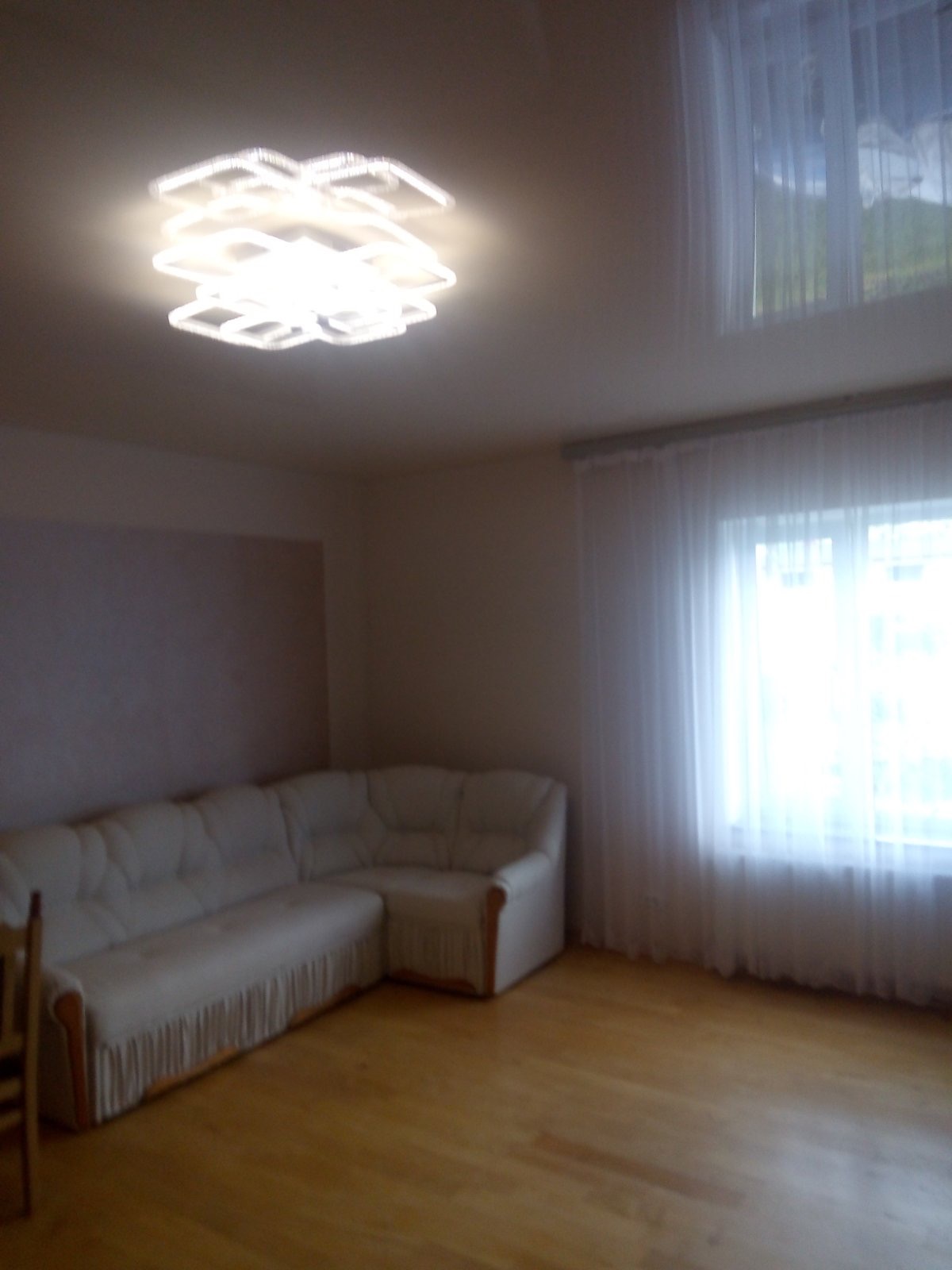 Jasny salon z narożną sofą z frędzlami, parkietem i nowoczesnym, geometrycznym plafonem