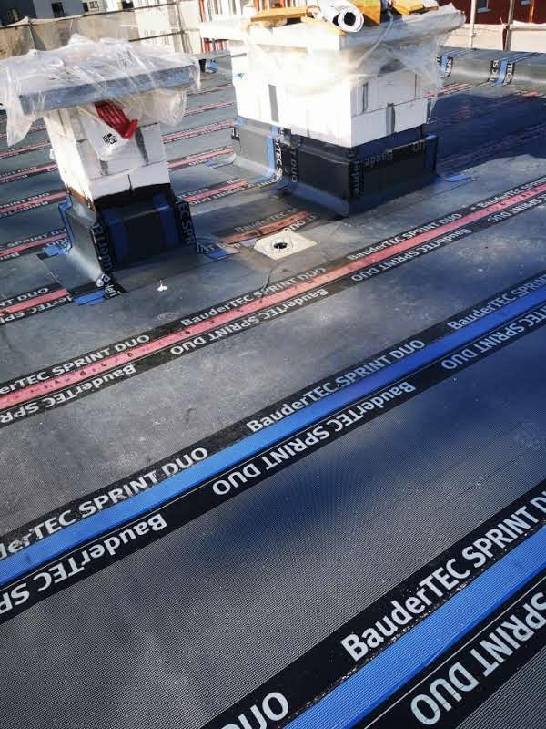 Dach pokryty papą termozgrzewalną BauderTEC SPRINT DUO, widoczne kominy zabezpieczone folią i cegłami, przygotowane do dalszych prac.