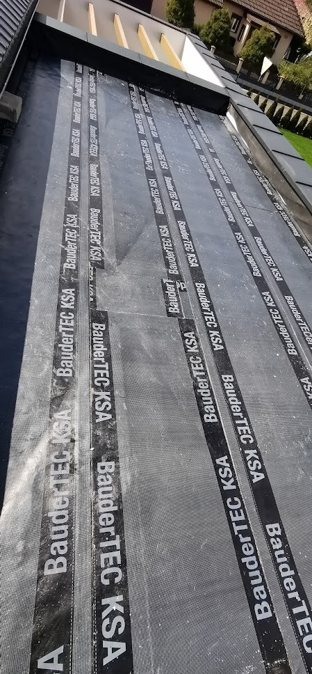 Nowo położona papa termozgrzewalna BauderTEC KSA na dachu płaskim, widok z góry, widoczne pasy papy z wyraźnym nadrukiem producenta.