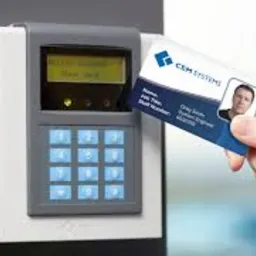 Pracownik zbliża kartę identyfikacyjną CEM Systems do czytnika kontroli dostępu zamontowanego na ścianie. Czytnik ma wyświetlacz LCD i klawiaturę numeryczną.