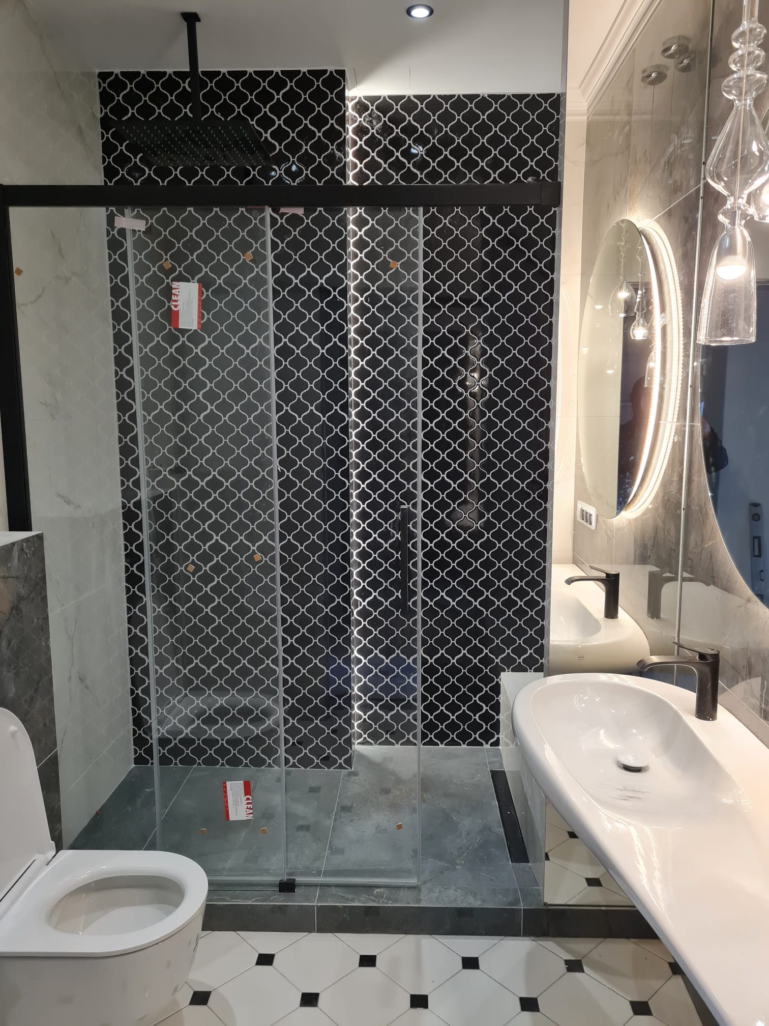 Nowoczesna łazienka z kabiną prysznicową typu walk-in, umywalką nablatową z czarną armaturą, lustrem z podświetleniem LED i dekoracyjnymi płytkami w geometryczny wzór.