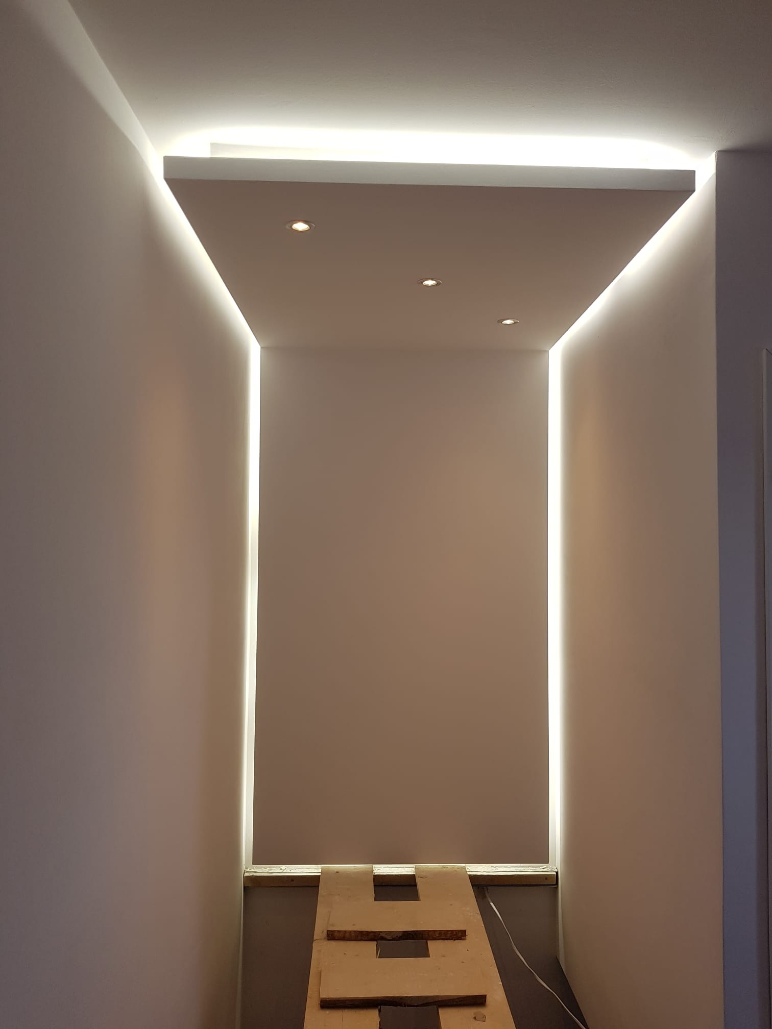 Wnęka z oświetleniem LED na suficie i ścianach, widoczne trzy punktowe lampy, zabezpieczona podłoga przed zabrudzeniem podczas prac wykończeniowych.