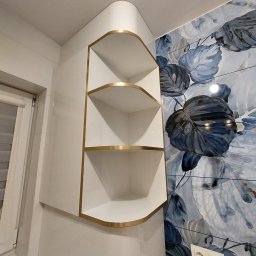 Hubert Czarkowski - Biała, narożna szafka z półkami i złotymi obramowaniami, zamontowana w kuchni z płytkami w kwiatowy wzór. Nowoczesny design i funkcjonalność.