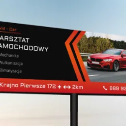 Billboard reklamowy warsztatu samochodowego David-Car z czerwonym sportowym samochodem, oferującego mechanikę, wulkanizację i klimatyzację, zlokalizowanego w Krajnie Pierwszym.
