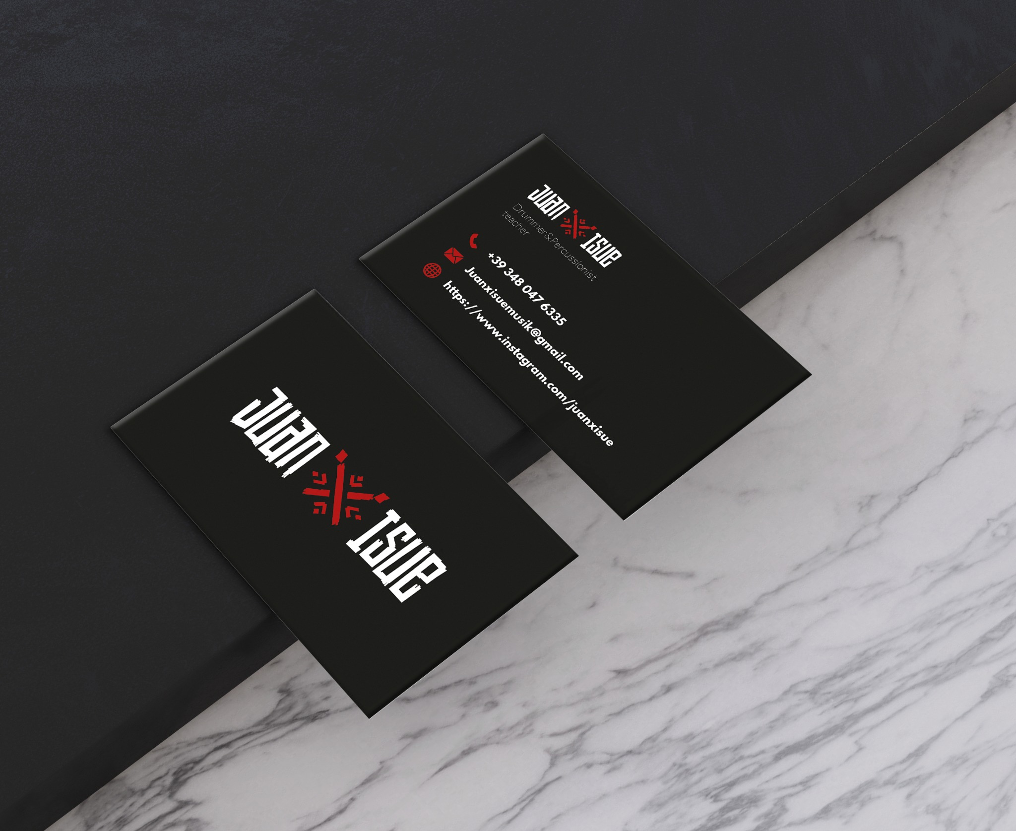 Dwie czarne wizytówki leżące pod kątem na marmurowym i czarnym tle. Wizytówki z białym napisem 'Juan X Isue' i czerwonym elementem graficznym, zawierają dane kontaktowe: numer telefonu, adres email...