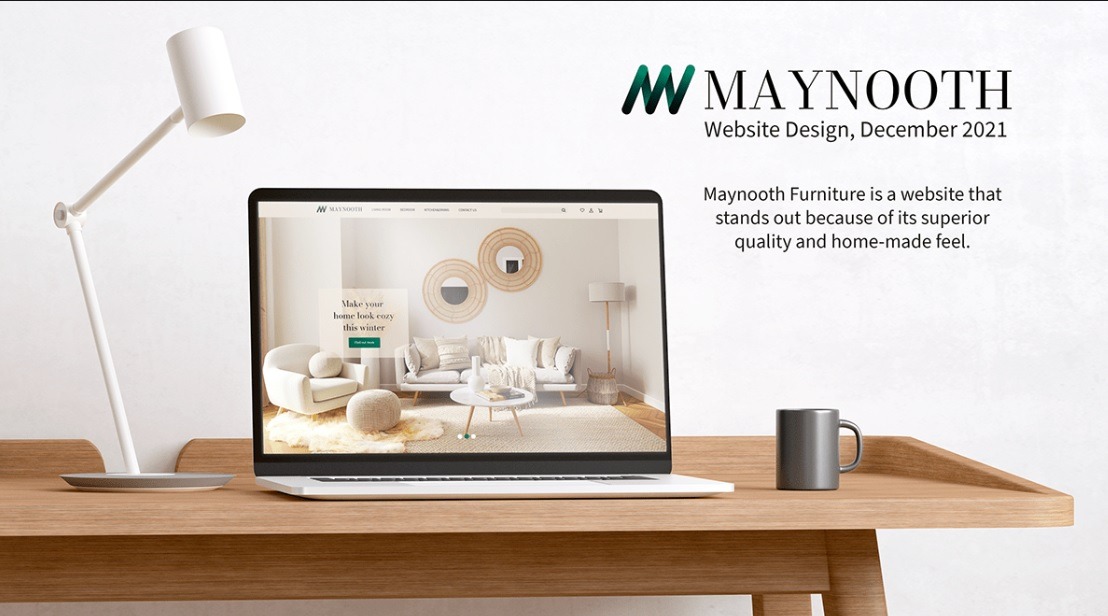 Laptop wyświetla stronę internetową Maynooth Furniture z aranżacją wnętrza w stylu skandynawskim, na biurku obok lampka i kubek.