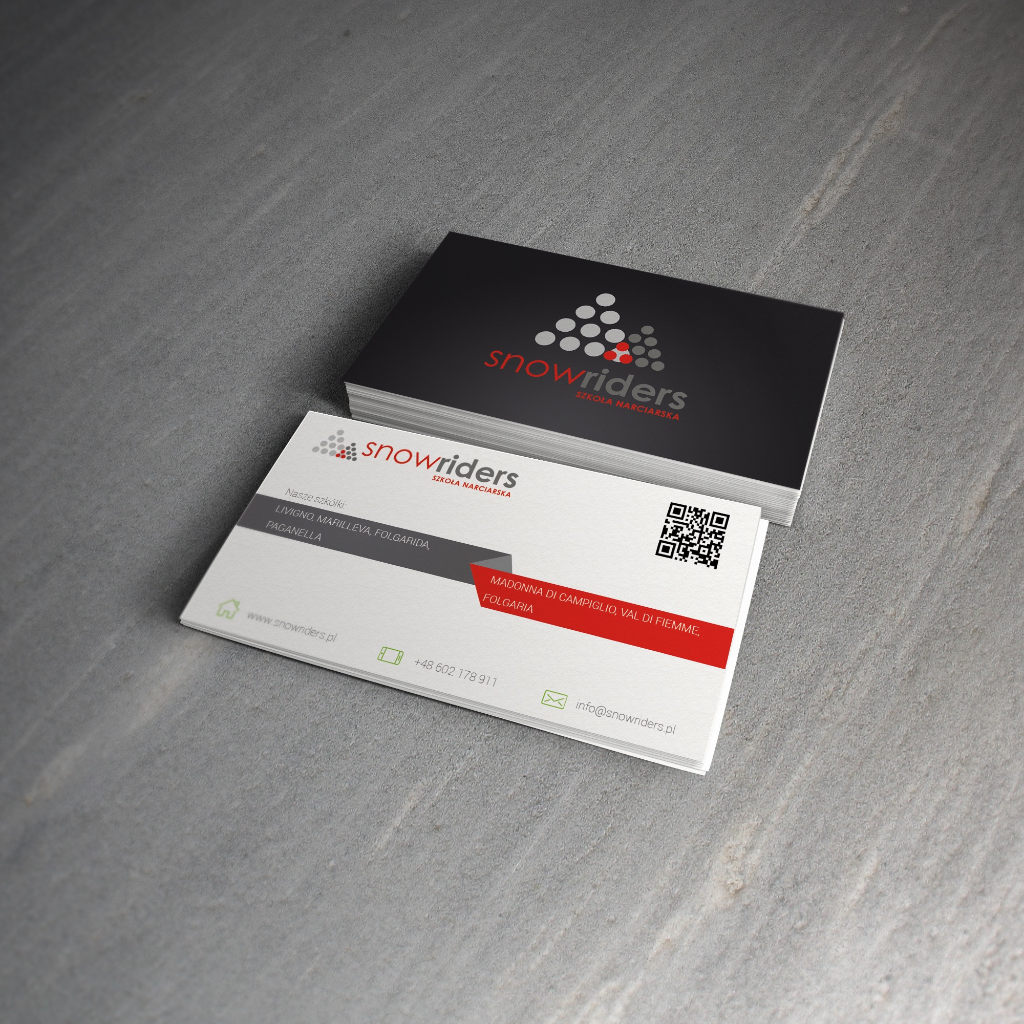 Stos wizytówek firmy Snowriders, szkoły narciarskiej, na szarym tle. Wizytówki w kolorystyce czarno-biało-czerwonej, z logo i danymi kontaktowymi.