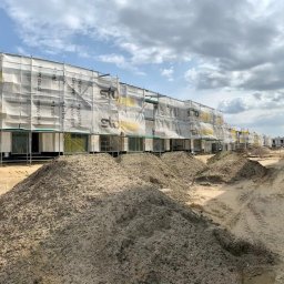 Velto - Wielorodzinny budynek w trakcie kompleksowego ocieplania, osłonięty siatką z logo Sto, widoczne rusztowania i hałdy piachu przed budynkiem.