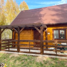 Easy Finish Michał Walczak - Drewniany dom z zadaszonym tarasem i brązowym dachem z blachy trapezowej. Widoczne narzędzia i materiały budowlane sugerują trwające prace wykończeniowe.