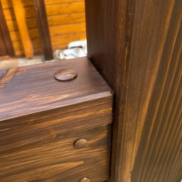 Easy Finish Michał Walczak - Detal drewnianej konstrukcji z ciemnego drewna, widoczne połączenia elementów za pomocą kołków. Element balustrady lub ogrodzenia, lakierowany na brązowo.