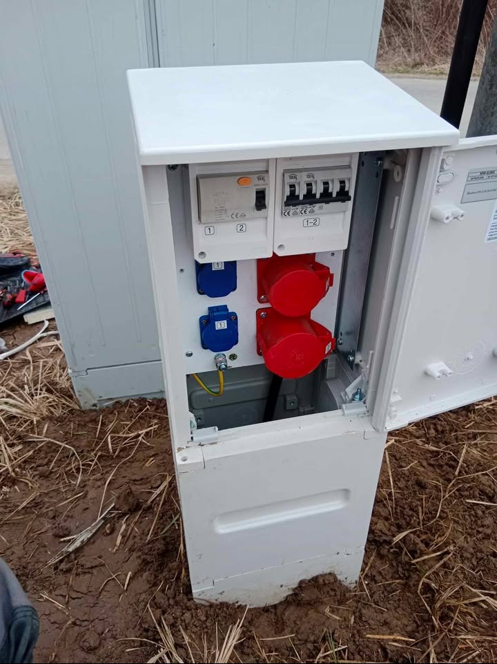 Tymczasowa rozdzielnia budowlana z gniazdami w Przegini. Biała skrzynka z zabezpieczeniami i gniazdami siłowymi, widoczne przewody i uziemienie. Zasilanie placu budowy.