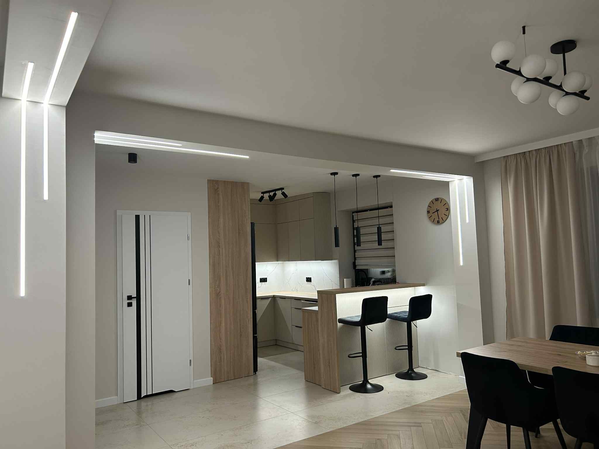 Nowoczesne oświetlenie LED w salonie z otwartą kuchnią, minimalistyczny design, podłużne lampy ścienne i sufitowe, eleganckie wykończenie wnętrza.