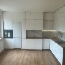 Kmeble usługi stolarskie Krzysztof Nowakowski - Nowoczesna, biała kuchnia z drewnianymi blatami i marmurowym panelem nad blatem, widoczne sprzęty AGD