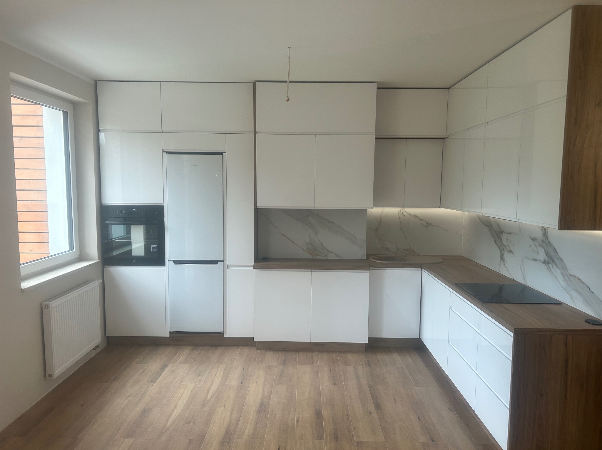 Nowoczesna, biała kuchnia z drewnianymi blatami i marmurowym panelem nad blatem, widoczne sprzęty AGD