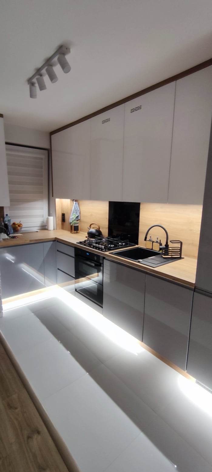 Nowoczesna kuchnia w szarościach z drewnianym blatem, oświetleniem LED pod szafkami i na podłodze, czajnik na płycie gazowej.