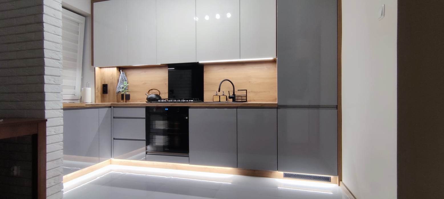 Szare, lakierowane meble kuchenne z drewnianymi akcentami, podświetleniem LED pod szafkami i na podłodze, czarny czajnik na płycie grzewczej, nowoczesne wzornictwo.