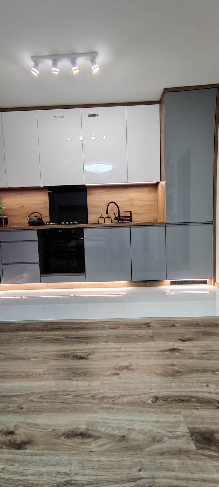 Nowoczesna kuchnia z szarymi i białymi szafkami, drewnianymi akcentami, podświetleniem LED i drewnianą podłogą.