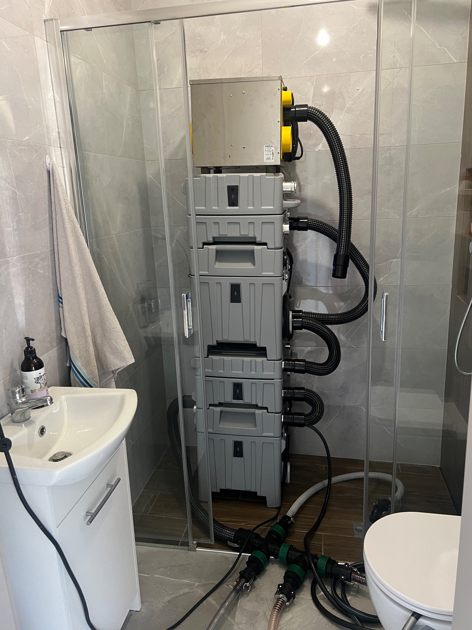 Profesjonalny sprzęt do osuszania w kabinie prysznicowej z szarymi płytkami. Widoczne węże, armatura i elementy instalacji. Domowe warunki.