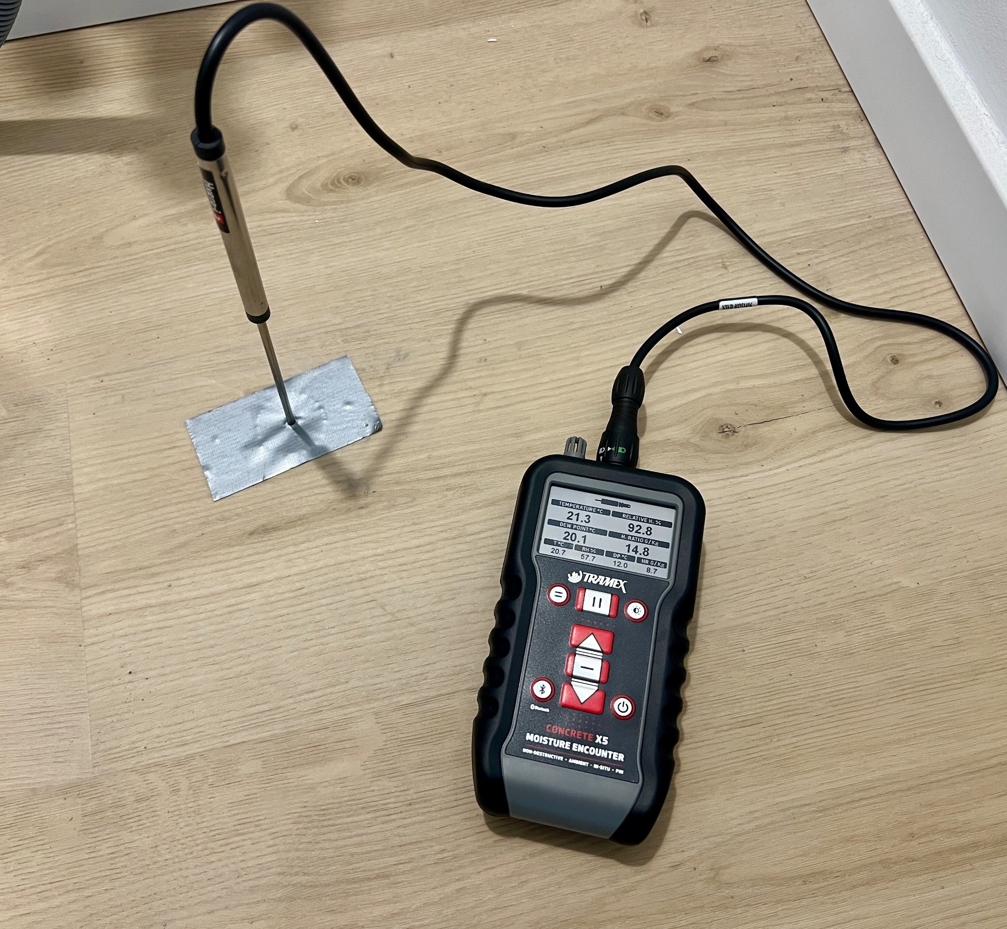Pomiar wilgotności posadzki w Poznaniu za pomocą wilgotnościomierza Tramex Concrete X5. Sonda wbita w podłogę, na ekranie urządzenia widoczne wyniki pomiaru.