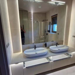 Andrii Maksymovych Ander-mar BUD - Nowoczesna łazienka z podwójną umywalką na blacie, podświetlana listwami LED, duże lustro z oświetleniem. Widoczne otwarte szuflady i beżowe płytki na ścianach.