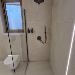 Andrii Maksymovych Ander-mar BUD - Nowoczesna łazienka z kabiną walk-in, czarną armaturą i podświetleniem LED. Minimalistyczny design, beżowe płytki. Widoczna toaleta pod oknem.