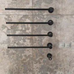 Ściana z płytek imitujących kamień z zamontowanym czarnym, drabinkowym grzejnikiem łazienkowym i włącznikiem światła. Minimalistyczny design.