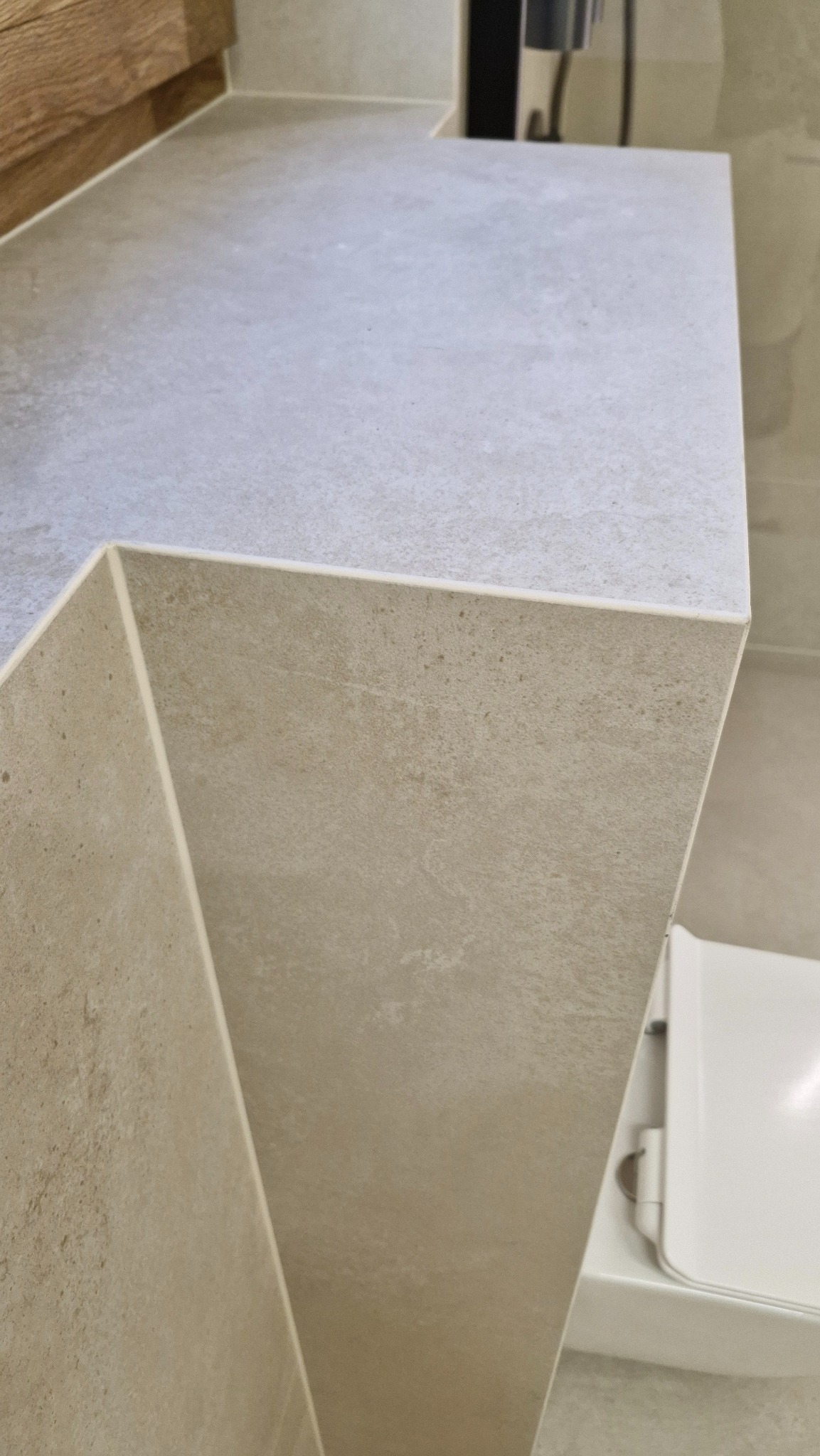 Beżowa, kamienna umywalka z blatem w łazience, z widocznym fragmentem toalety. Ujęcie z góry podkreśla fakturę materiału i minimalistyczny design.