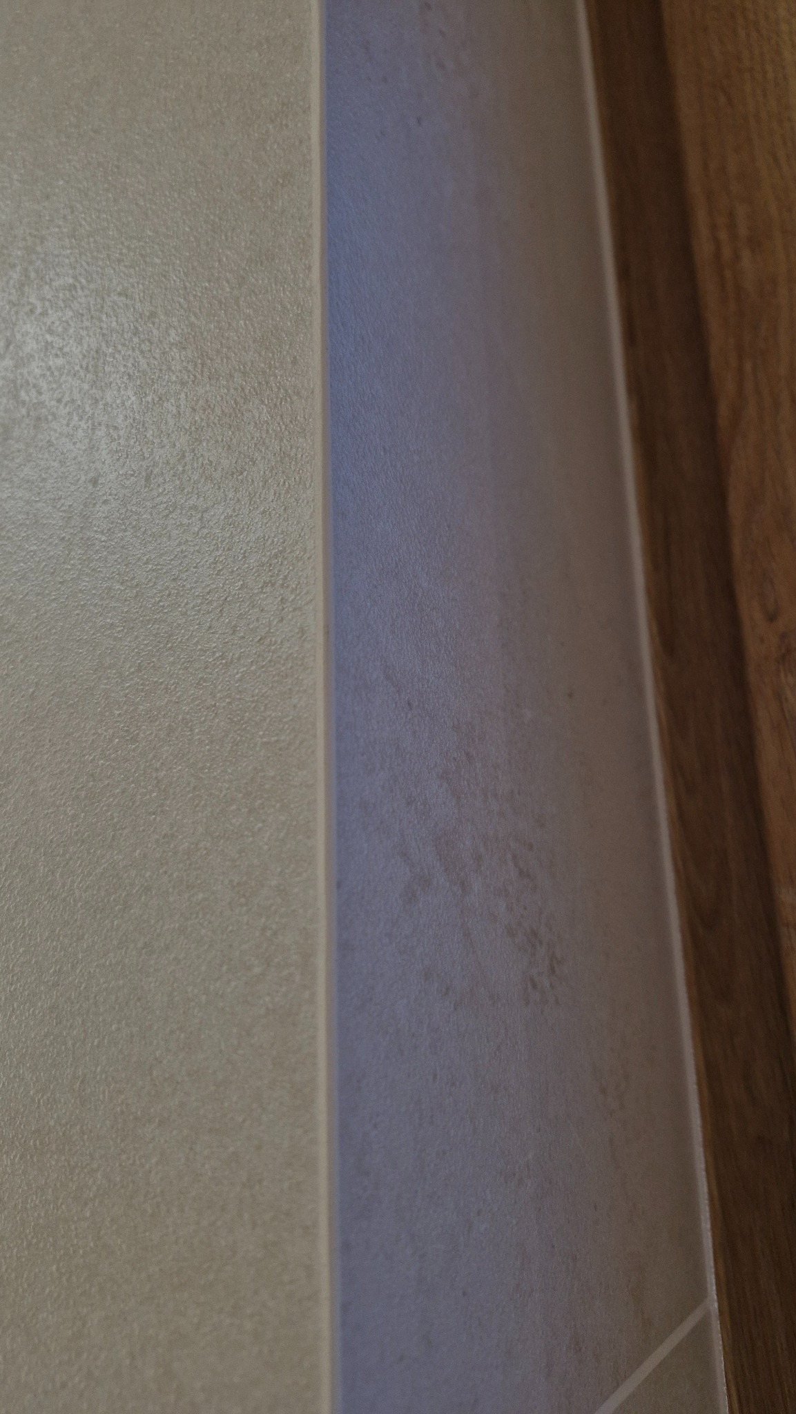 Detal wykończenia narożnika łazienki: połączenie beżowych płytek z delikatną fakturą i drewnopodobnej okleiny, tworzące eleganckie i nowoczesne wnętrze.