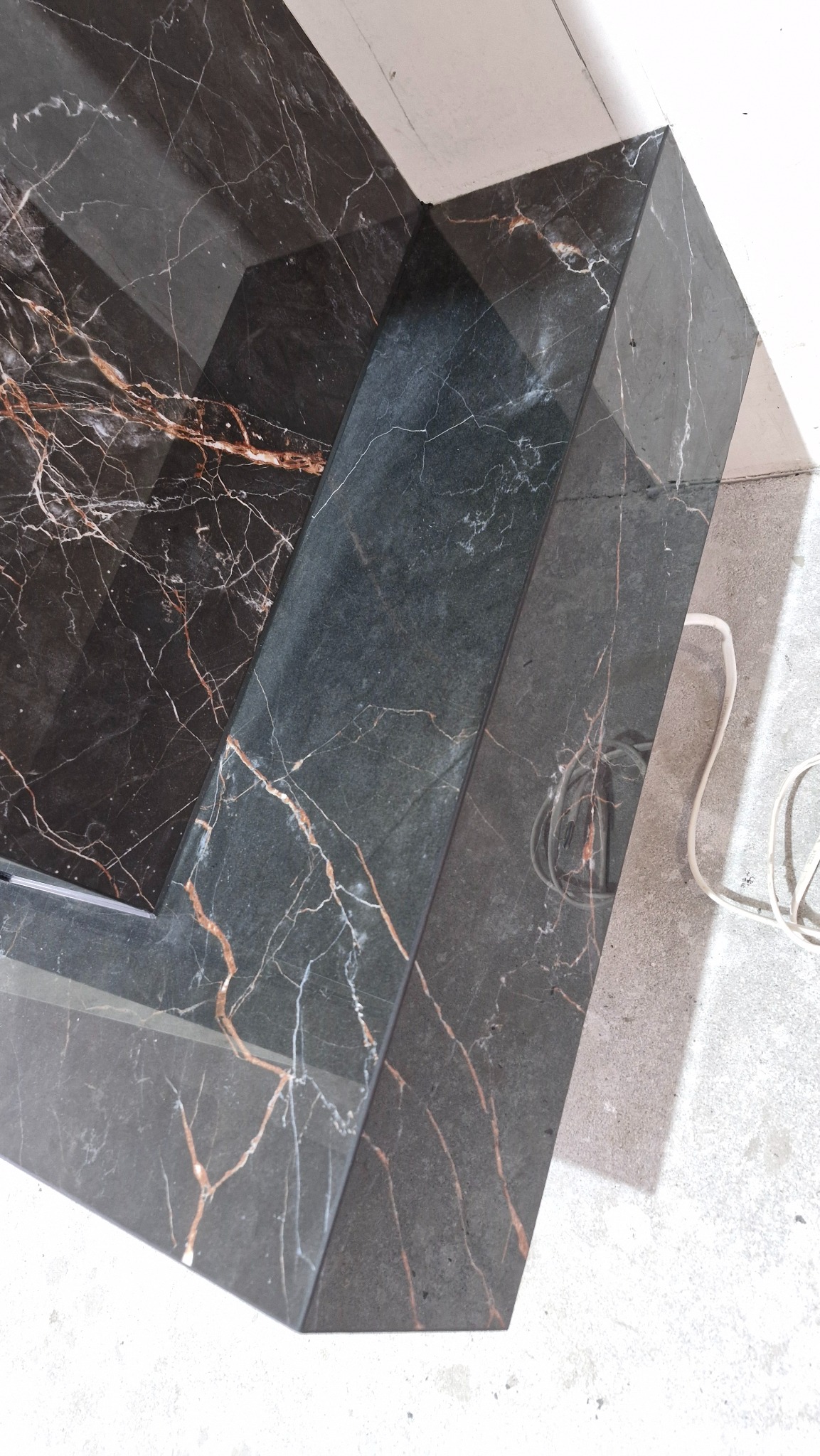 Wykończony fragment blatu z czarnego marmuru z wyraźnym, brązowym użyleniem. Ułożony na podłodze, z widocznym kablem elektrycznym w tle.