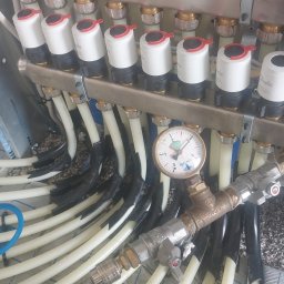 Instalatorstwo grzewcze LR LESKAROMA - Rozdzielacz ogrzewania podłogowego z manometrem, widoczne rury grzewcze w izolacji, przed wylaniem wylewki.