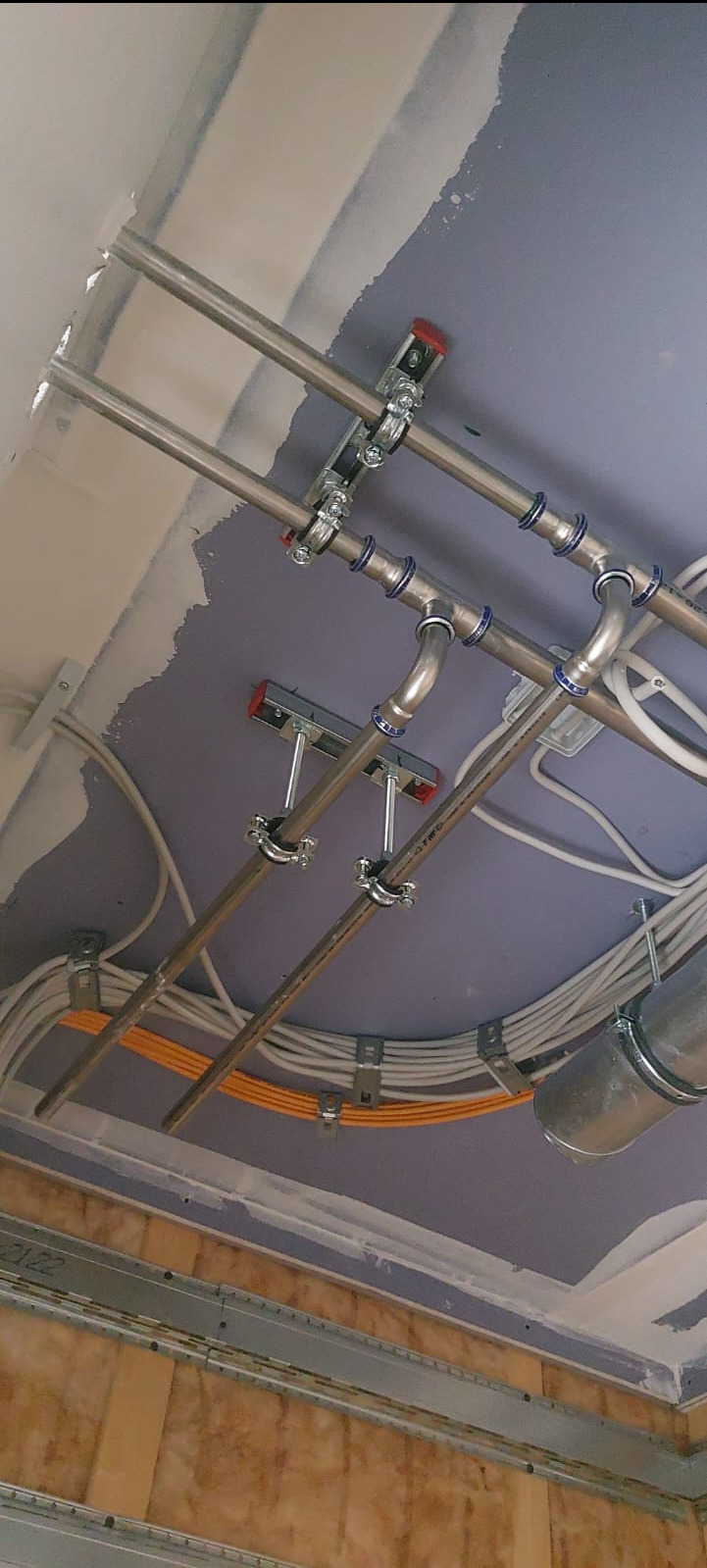 Instalacja rur miedzianych pod sufitem podwieszanym z widocznymi kablami elektrycznymi i elementami mocującymi.