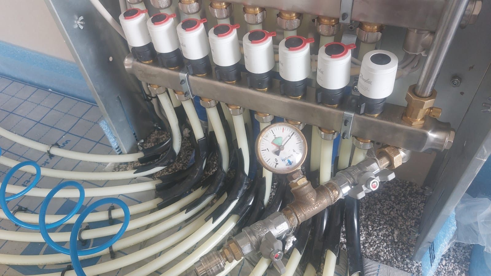 Rozdzielacz ogrzewania podłogowego z manometrem, widoczne rury grzewcze w izolacji, przed wylaniem wylewki.